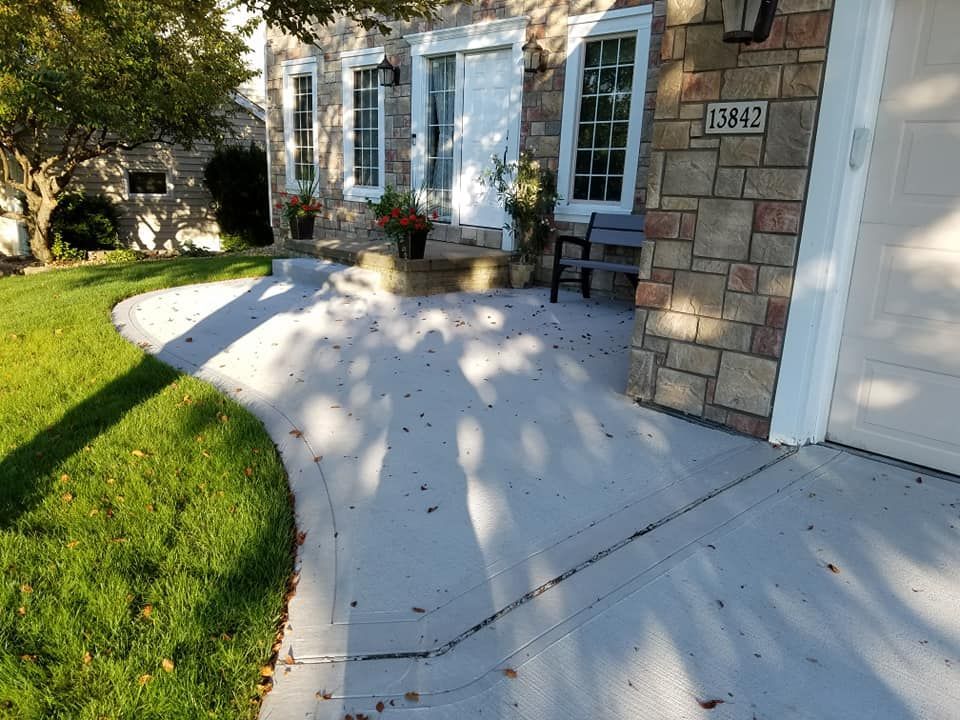 Concrete walkway leading to a house with stone siding and a white garage door; green lawn on the left.