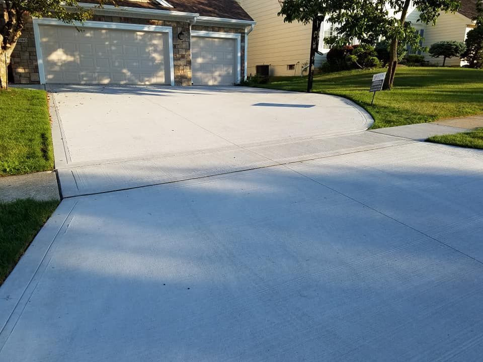 Gray concrete driveway leading to a house with a garage and green lawn.