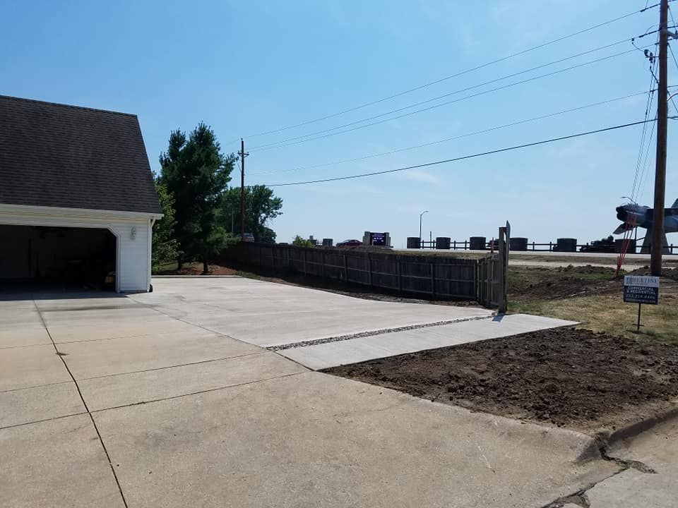 Driveway with a garage on the left, leading to a wooden fence and roadside. Blue sky above.