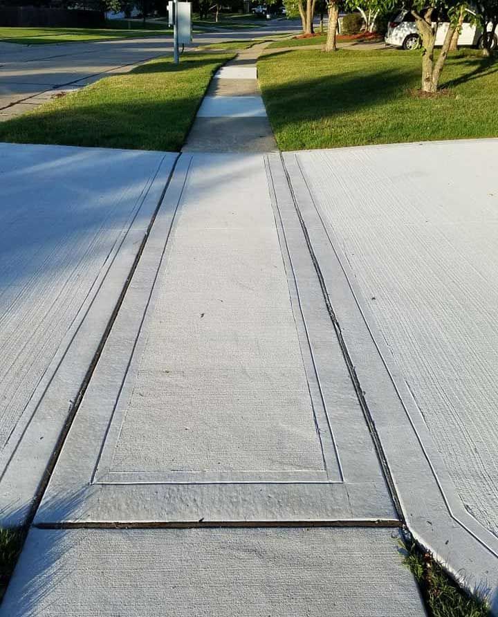 Concrete sidewalk with grassy areas on both sides, leading toward a street in a suburban setting.