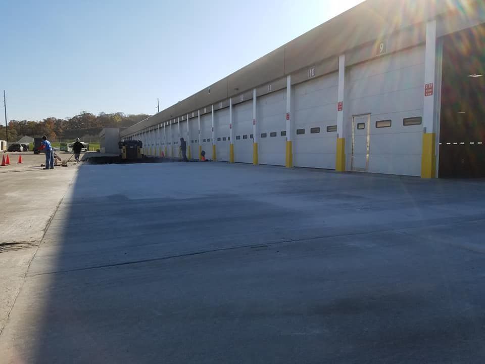 Exterior view of building with many garage doors, workers, and a freshly paved area.