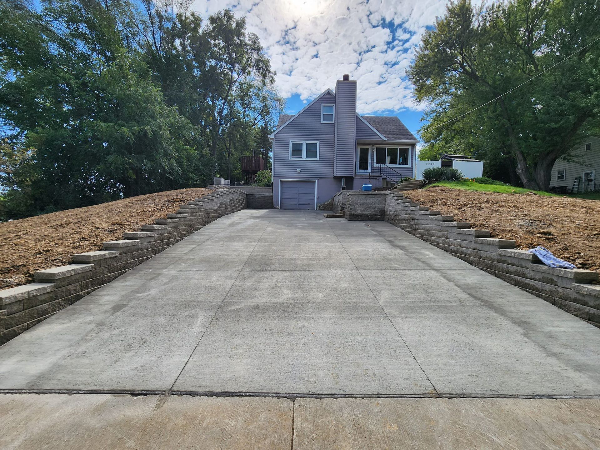 Gray house with driveway flanked by retaining walls. Overcast sky.