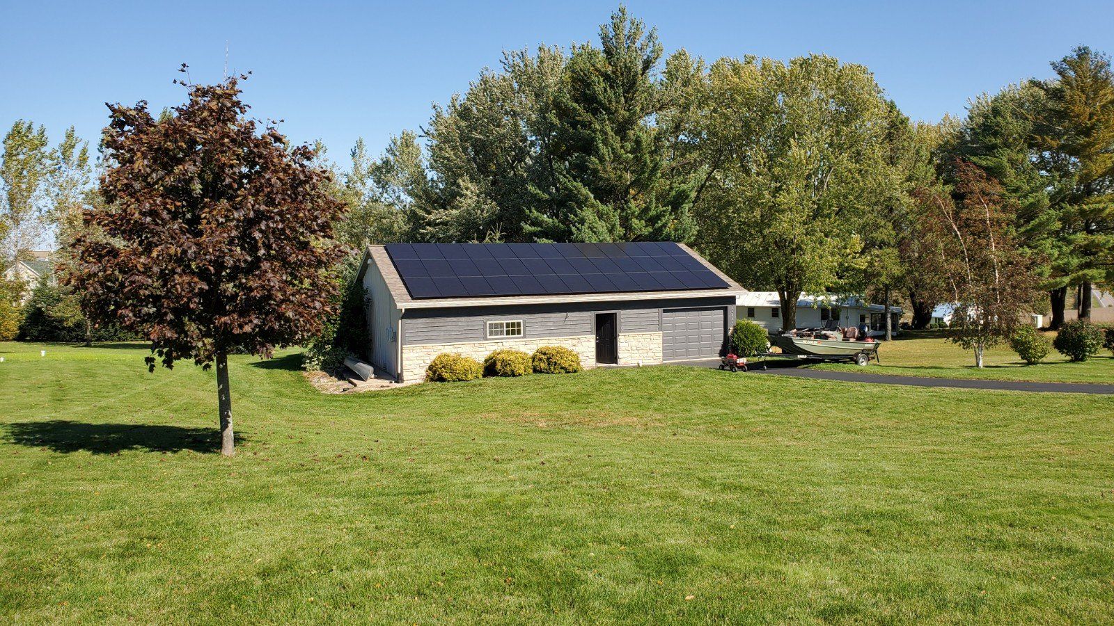 A garage with solar panels on the roof is sitting in the middle of a lush green field.