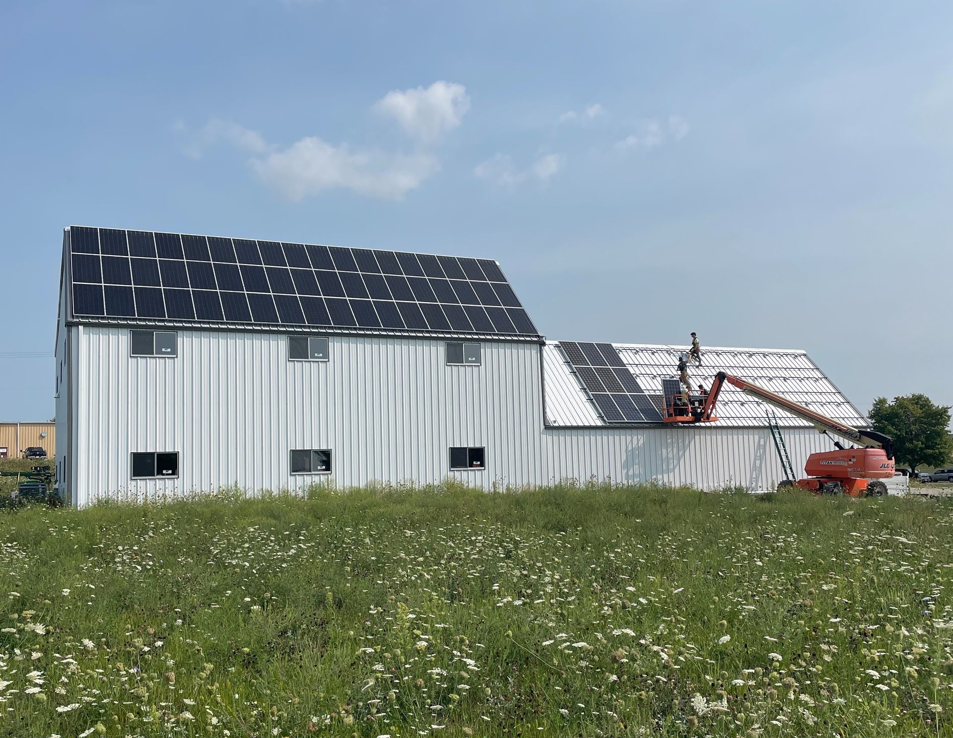 Solar panels being installed on Ethos Green Power Cooperative Headquarters in Viroqua, Wisconsin. Workers install with a telehandler under blue skies with wildflower field in the foreground.