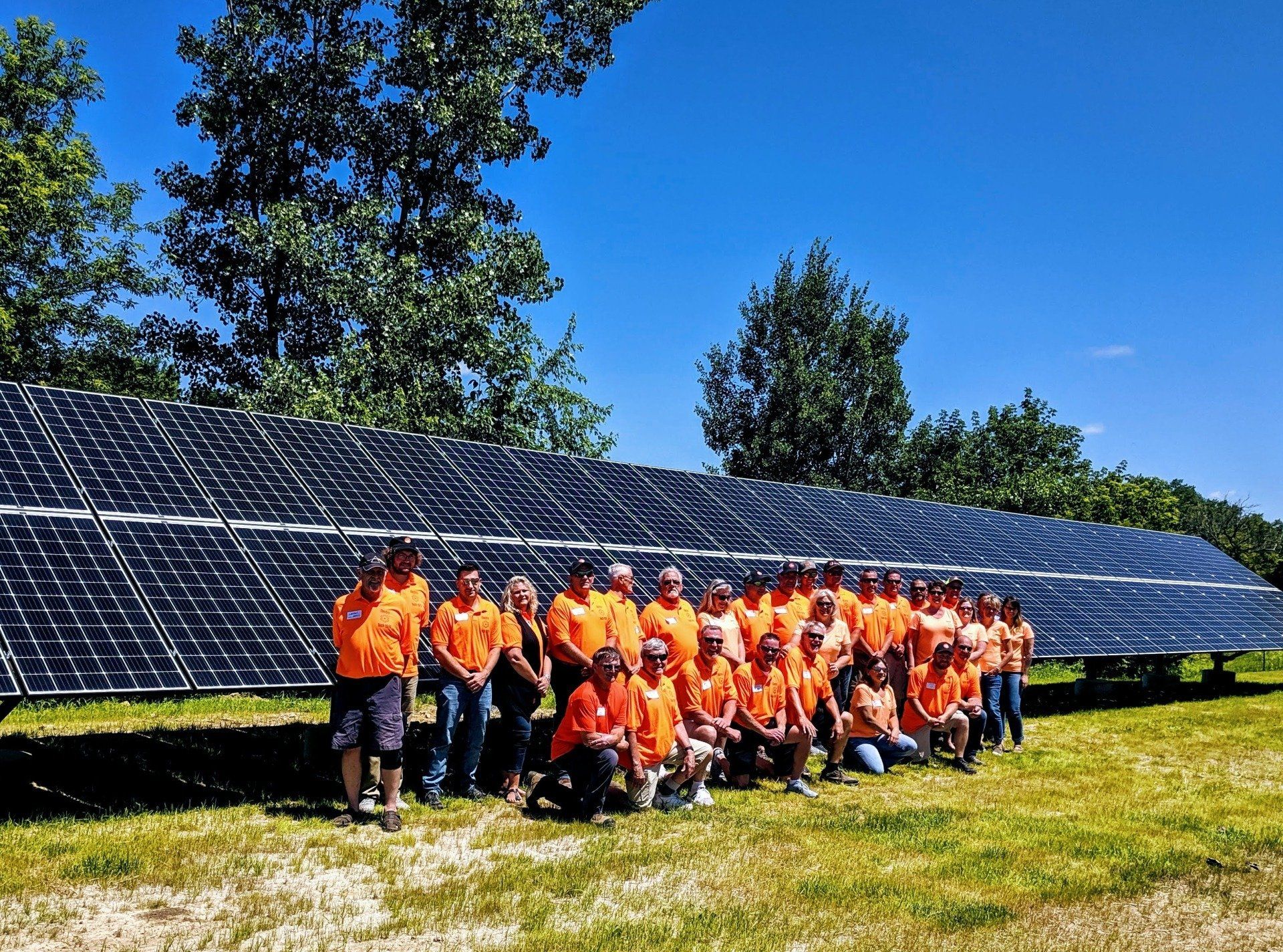 A large group of people are posing for a picture in front of a row of solar panels.