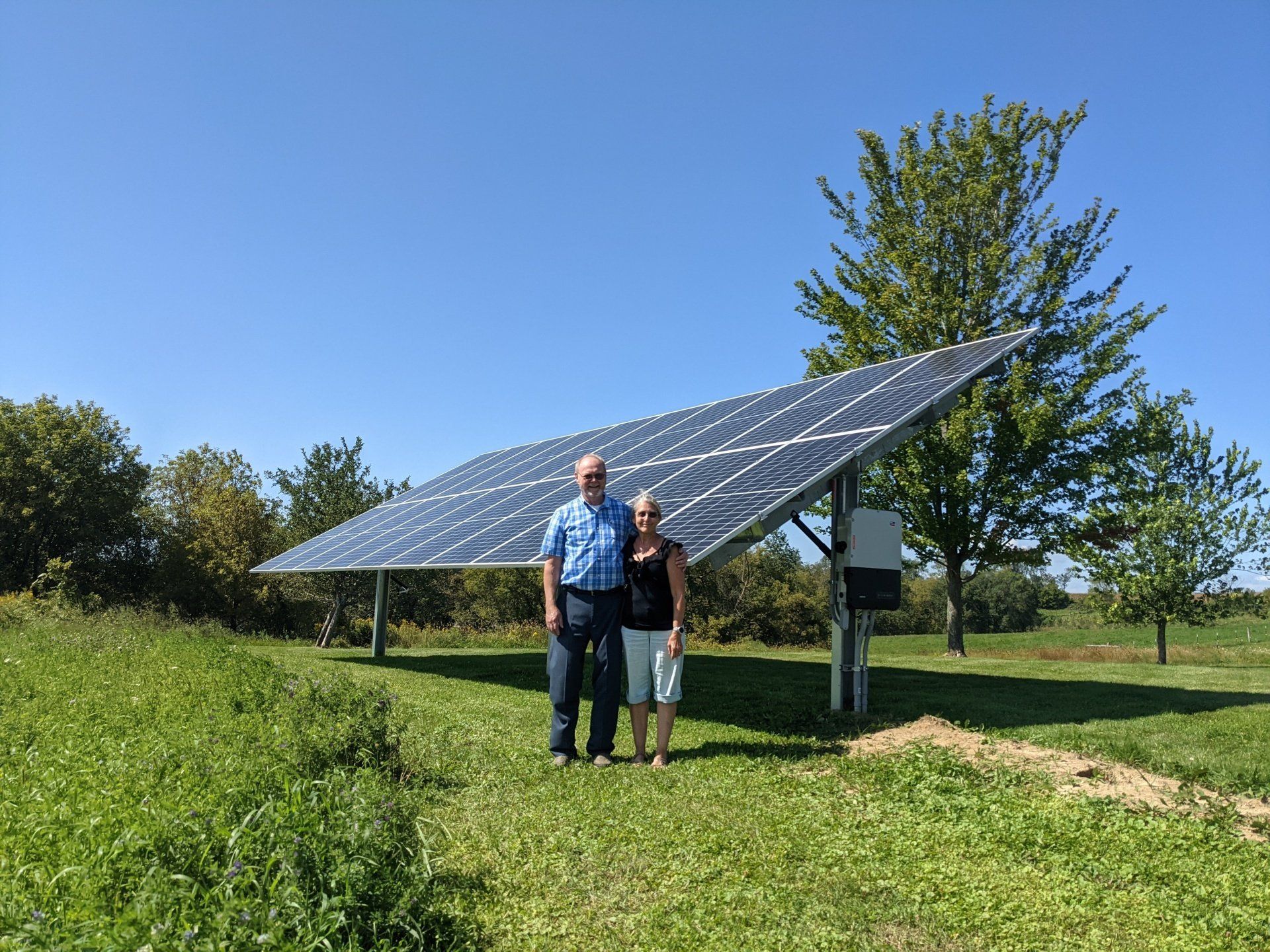 A man and a woman are standing in front of a large solar panel.