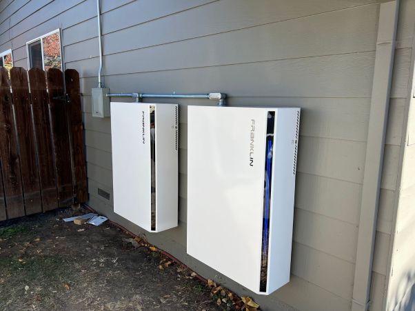 Two white batteries are mounted on the side of a house