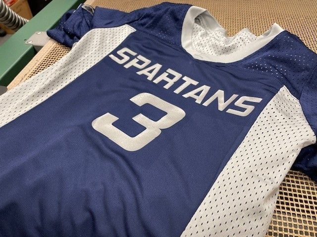 Blue-and-white Spartans jersey with number 3 laid flat on a surface