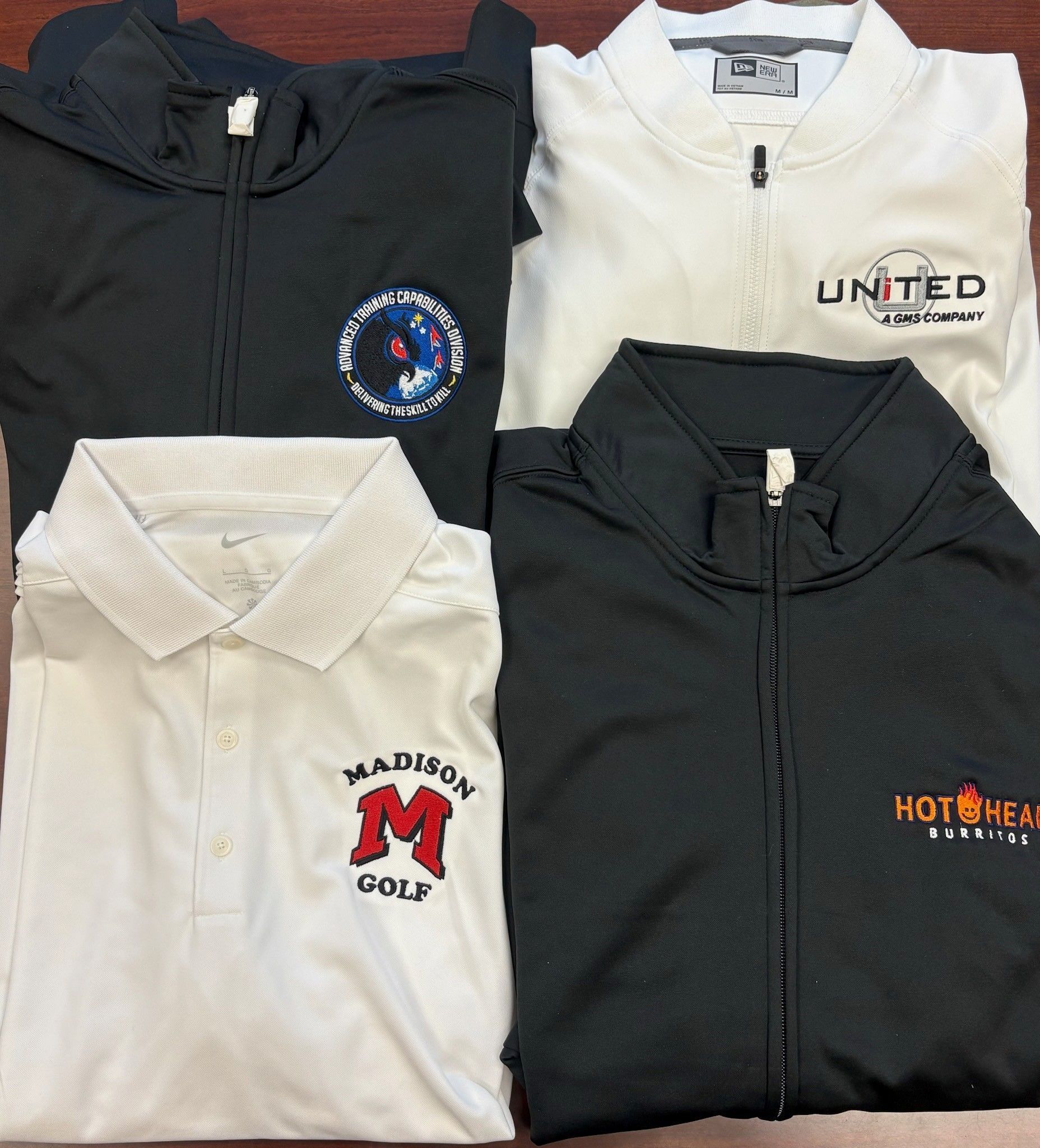 Four folded collared shirts in black and white with embroidered logos arranged in a 2x2 grid.
