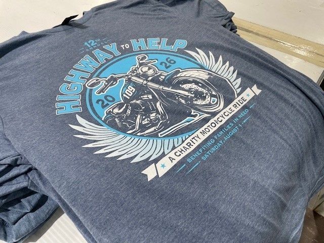 Blue T-shirt with a motorcycle graphic and “Run to Help” text laid on a surface