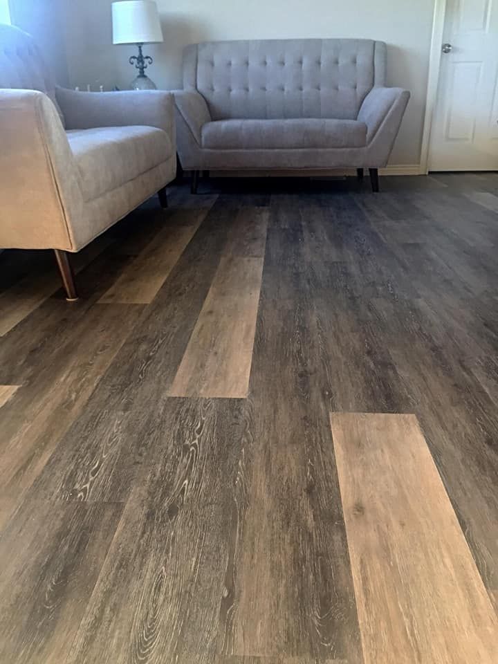 Living room with light-colored couch, loveseat, and wood-look flooring. A lamp and door are visible.