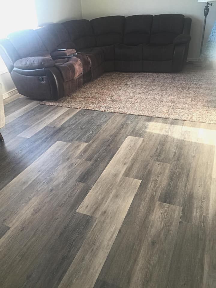 A brown sectional sofa and a tan rug sit on gray wood-look flooring.
