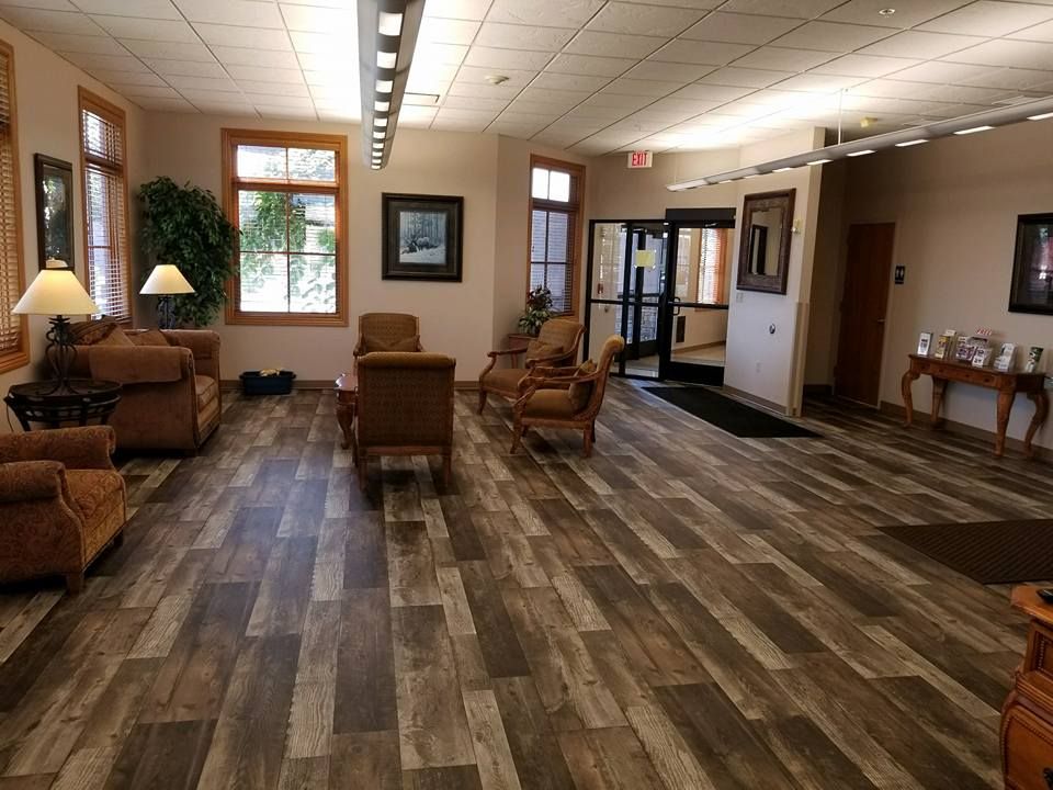 Lobby with wood-look floors, comfortable seating, windows, and an exit door. Warm color palette.