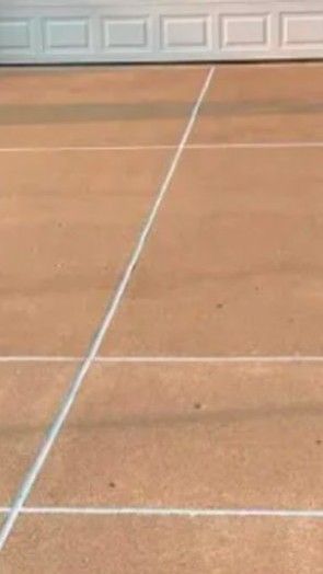 Tennis court with white lines on a brown surface, a white wall is in the background.