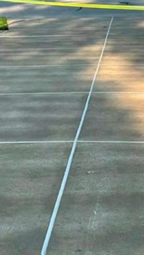 White painted line on a concrete surface, with a yellow barrier in the upper background.