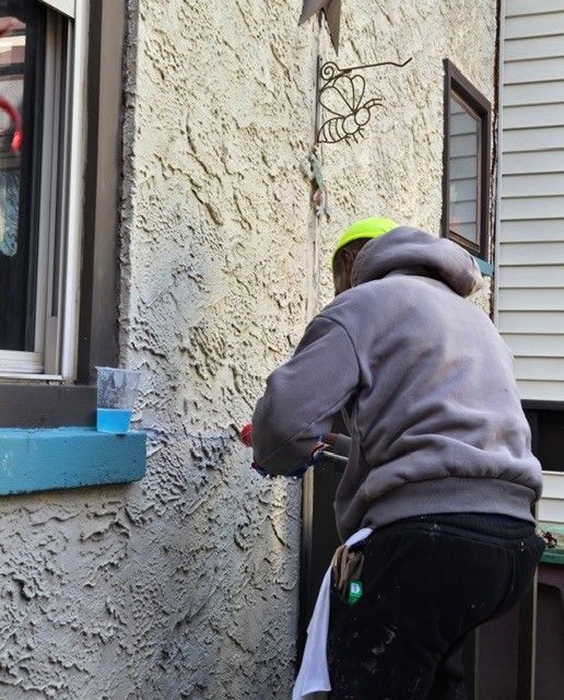 Person painting stucco exterior wall with roller.