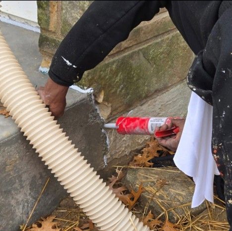 Person applying caulk to concrete steps with a red caulk gun, near a corrugated tube.