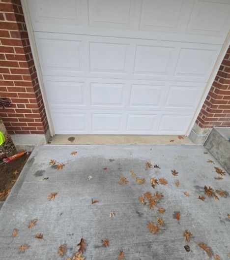 White garage door above a concrete slab scattered with brown leaves, between brick walls.