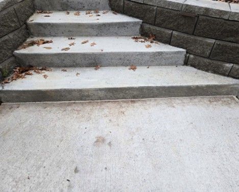 Concrete stairs with scattered brown leaves, leading up to a stone wall.
