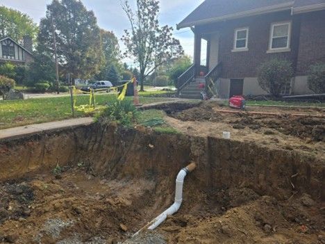 Excavation in front yard of a brick house. White pipe extends from the ground.