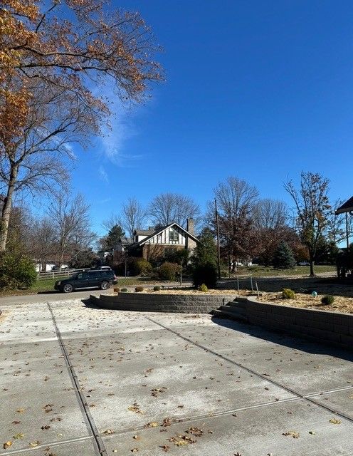 Exterior view of a driveway with a small tiered garden and a house in the background under a bright blue sky.