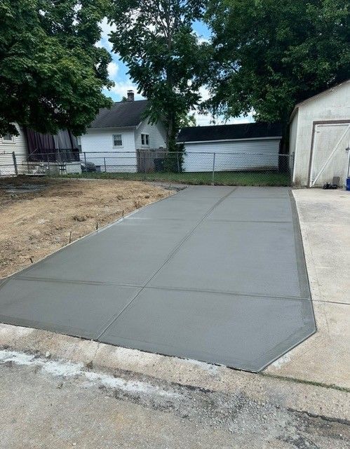 Newly poured concrete driveway with saw cuts, set in a yard. Grey with a slight sheen.