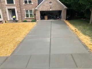 Newly poured concrete driveway in front of a brick house with an open garage.