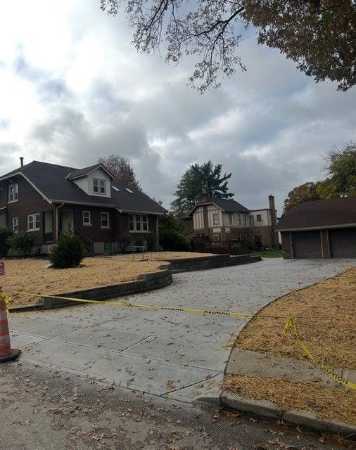 A two-story brick house with a newly paved driveway and detached garage under a cloudy sky.