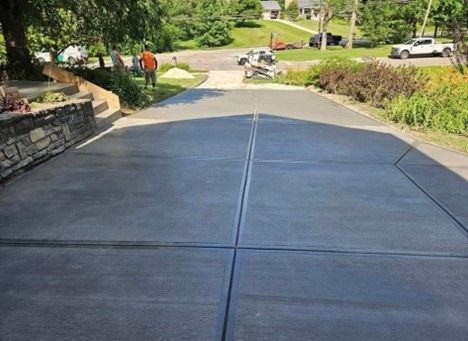 Newly poured concrete driveway with a man standing at the top, houses and landscaping in the background.