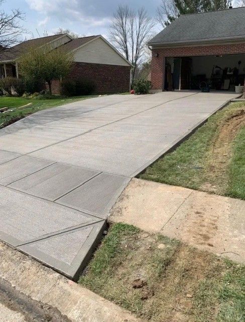 Newly poured concrete driveway with a triangular transition to the sidewalk and garage visible.