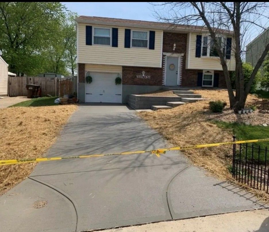 House with gray driveway, beige siding, blue shutters. Steps lead to the front door. Yellow caution tape across driveway.