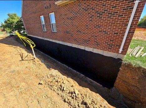 A foundation of a brick building with a newly excavated trench. Black waterproof coating is visible.