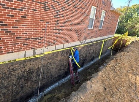Construction worker in a trench next to a brick building. Yellow caution tape surrounds the area.