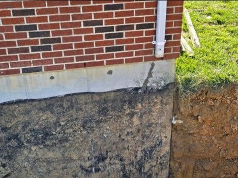 Brick house foundation with exposed soil, crack in concrete.