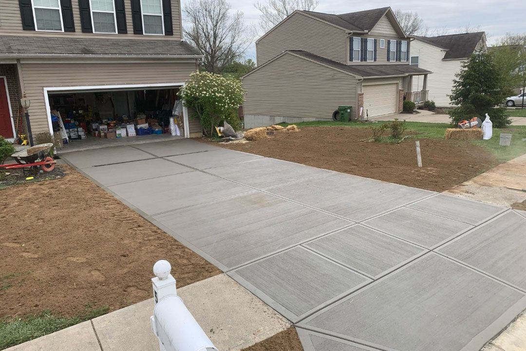 Concrete driveway leading to a two-story house with an open garage. Brown yard and another house in the background.