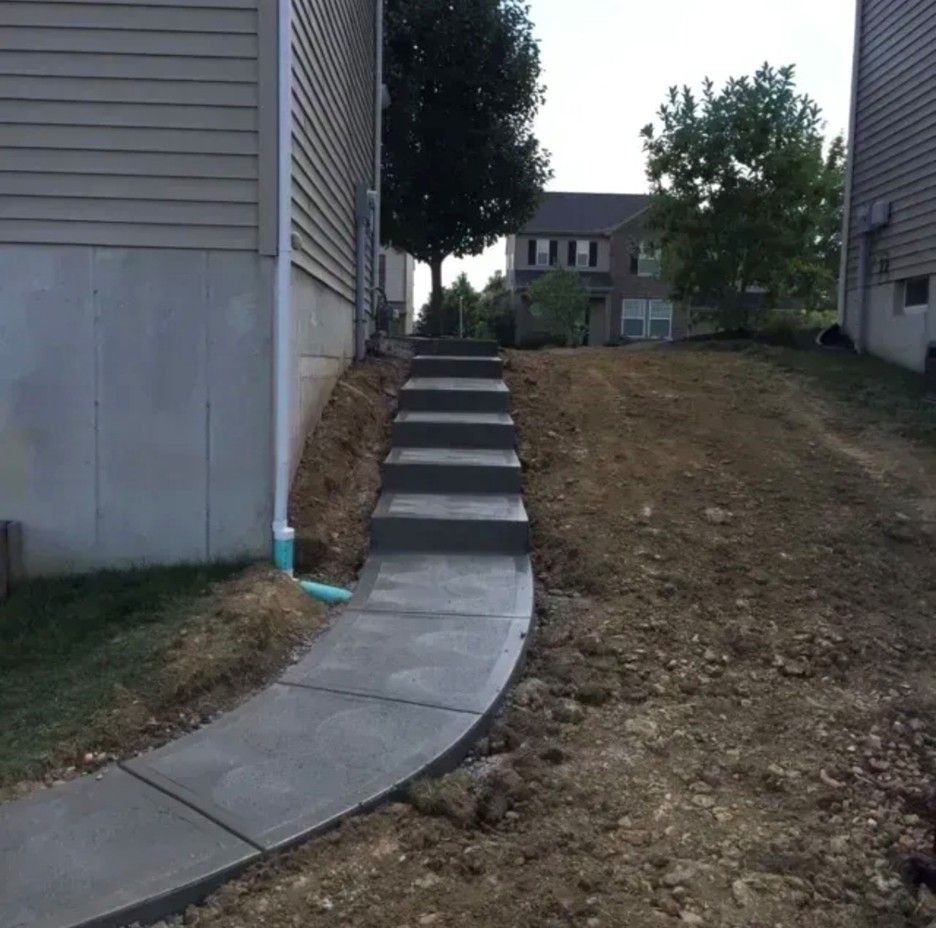 Concrete steps and walkway ascend a grassy hill between two buildings, leading to a distant structure.