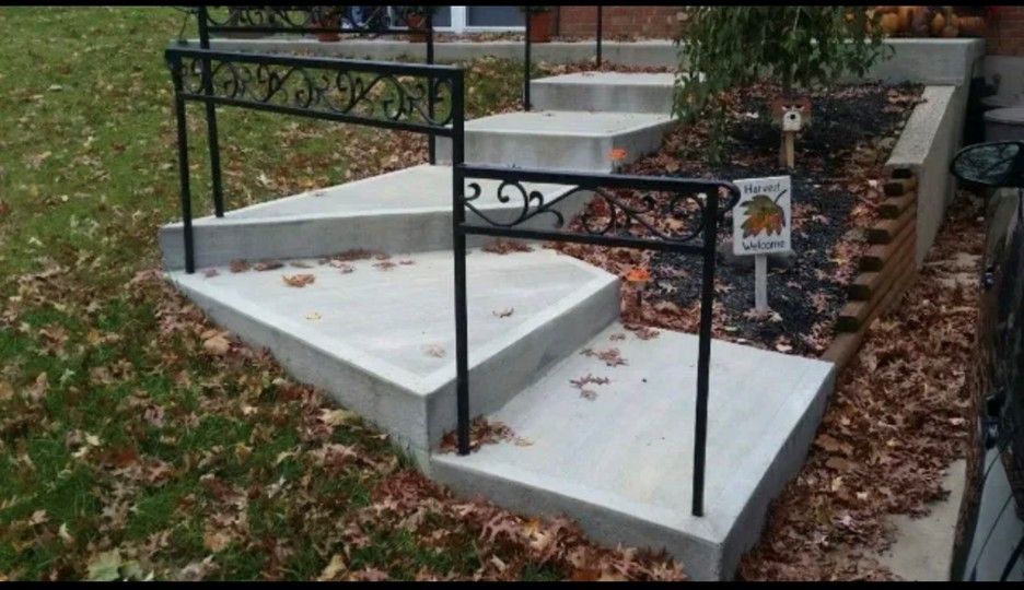 Concrete steps with black metal railings in a yard covered in fallen leaves.