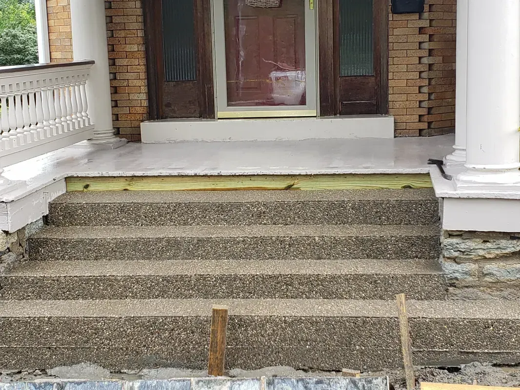 Concrete steps leading up to a house entrance with stone facade, under construction.