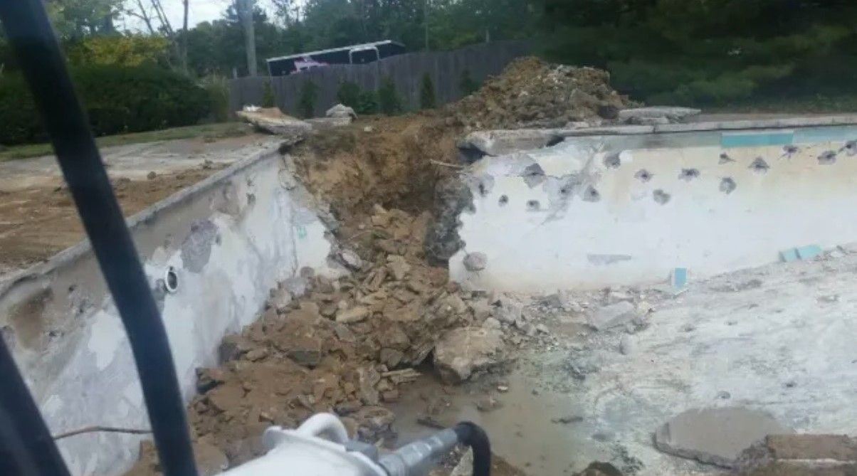 Demolished swimming pool with debris, concrete, and earth.