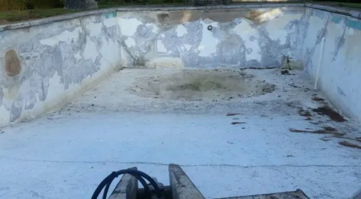 Empty, weathered swimming pool with peeling paint and debris.