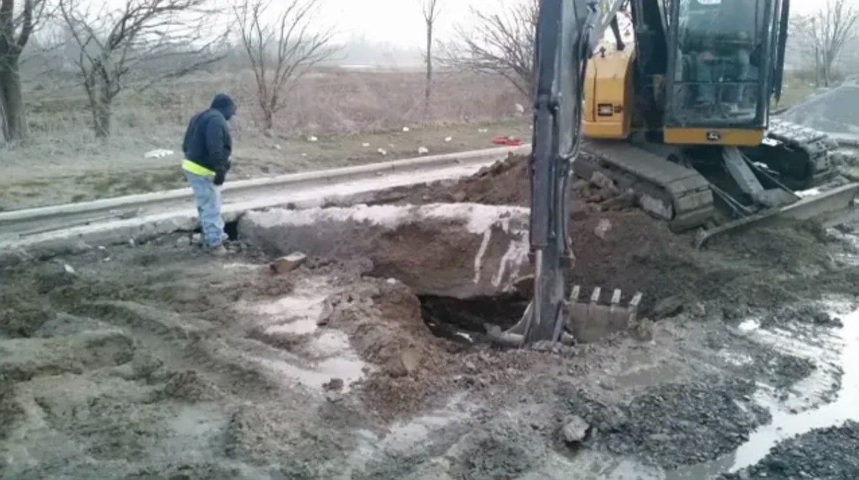Man observing a construction site with excavator digging near a railroad track. Muddy ground, overcast day.