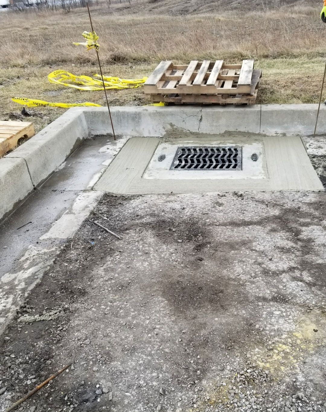 Concrete construction site with a drainage grate. Pallets and yellow caution tape in the background.