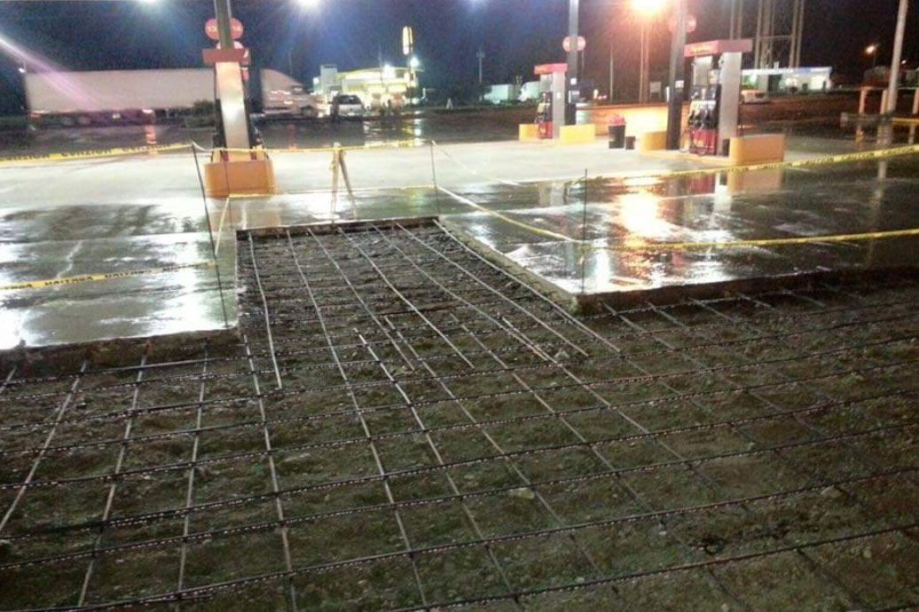 Gas station concrete repair. Metal rebar grid laid on ground, wet pavement, night.