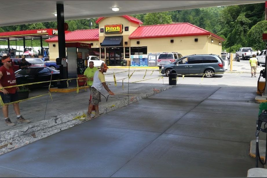 Gas station concrete work in progress, workers, caution tape, cars, and a Denny's restaurant in the background.
