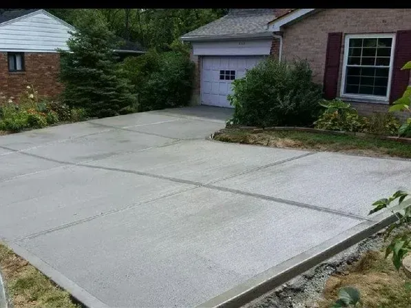 A newly poured light-gray concrete driveway leading to a house with a garage and a brick exterior.