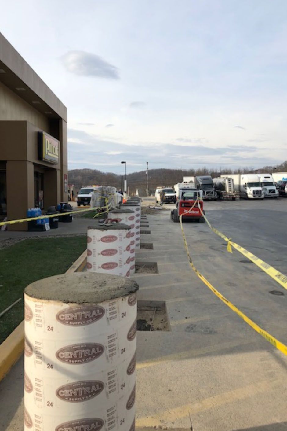 Concrete bollards being installed in front of a building; a construction area with yellow caution tape.