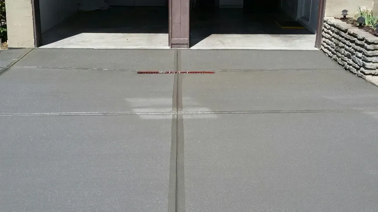 Freshly poured, gray concrete driveway with a drain leading to a garage.