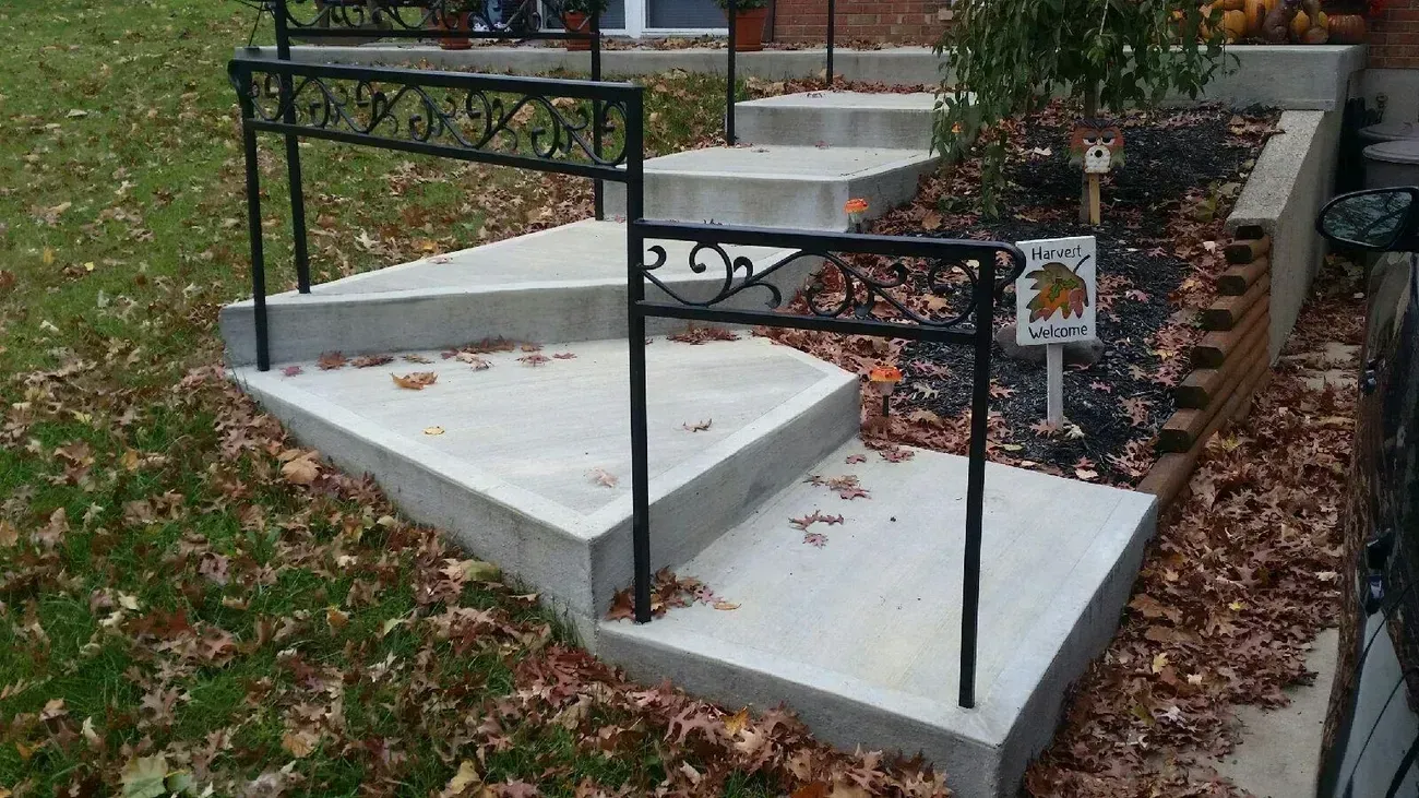 Concrete steps with black wrought iron railing in a yard with fall leaves.