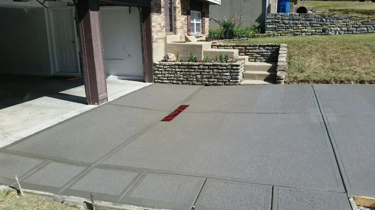 Freshly poured gray concrete driveway with cuts, near a house with steps.