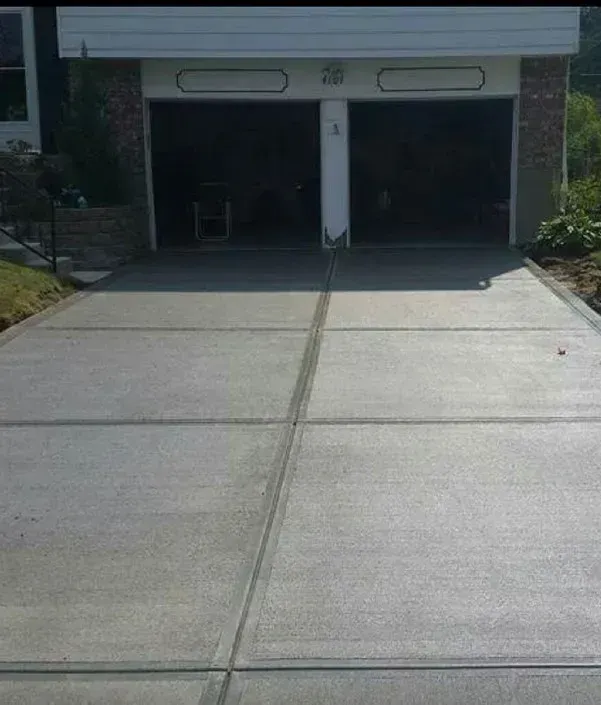 New concrete driveway leading to a two-car garage with brick accents and open doors.